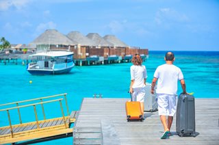 couple walking on a dock with luggage next to the ocean