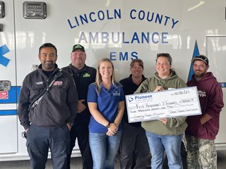 woman holding a large check with other people standing around her, ambulance in the background
