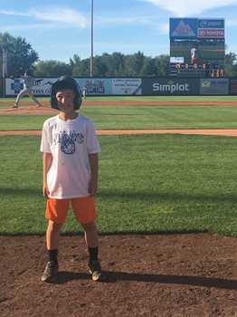 young boy standing on a baseball field wearing a hat and a Boise Hawks shirt