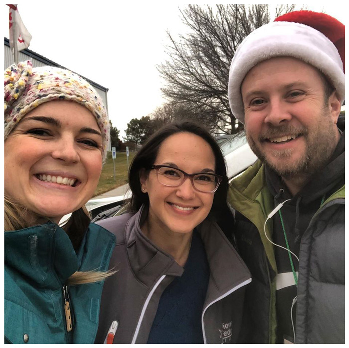 three smiling people, one wearing a Santa hat