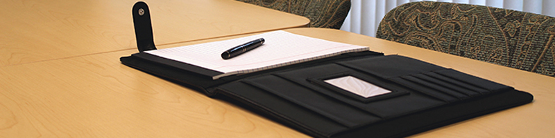 Professional portfolio with pad of paper and pen on top at a meeting room table