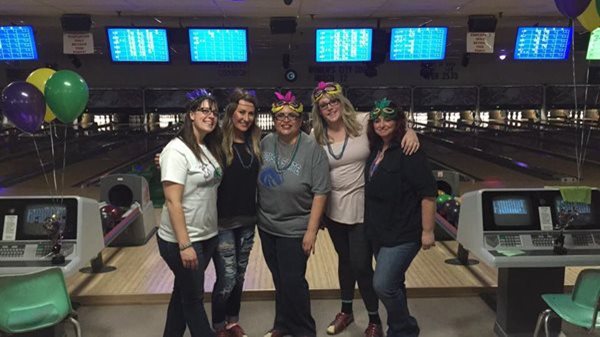 Five women wearing masquerade masks in front of bowling alleys