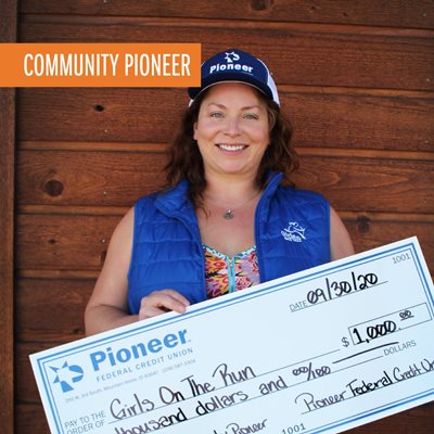 woman wearing a blue hat and vest holding a large check