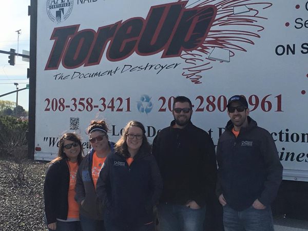 Five adults standing in front of a paper shredder truck