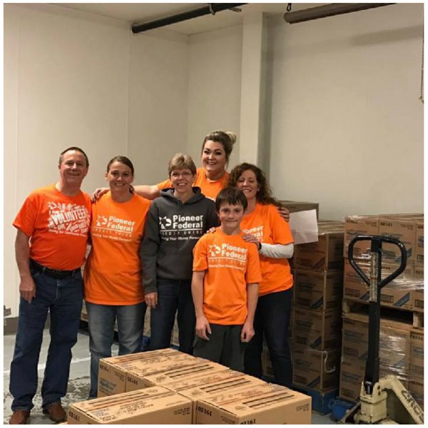 Six volunteers at a food bank standing in front of boxes full of food