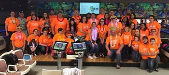 large group of people wearing orange shirts in front of bowling lanes