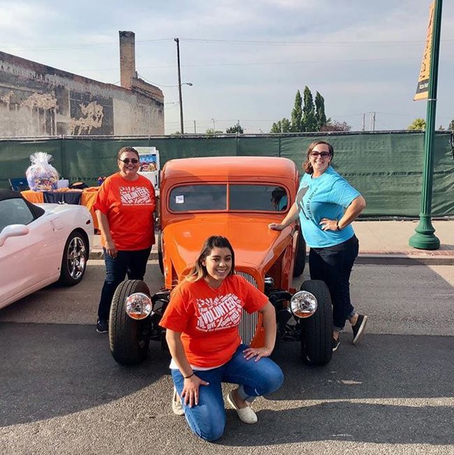 Three Pioneer volunteers posing with a orange hotrod.