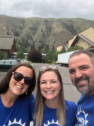 three employees smiling with a mountain behind them