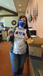 woman wearing a mask holding a piece of paper that says Power Up!