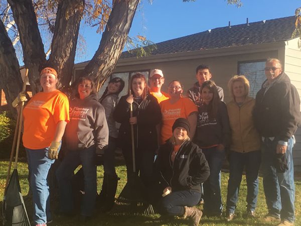 Pioneer volunteers with a few holding rakes after raking up leaves in a backyard