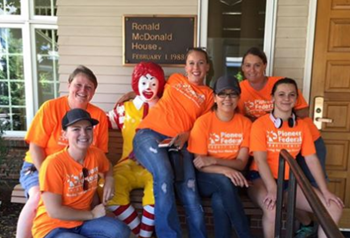 six women wearing orange shirts in front of the Ronald McDonald House