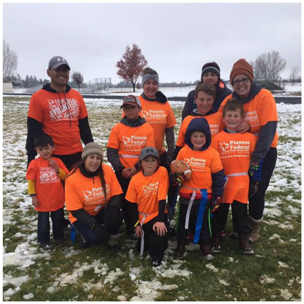 Kids and adults wearing orange volunteer shirts standing in a snowy field after playing flag football