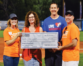 three smiling adults and one winner holding a giant check