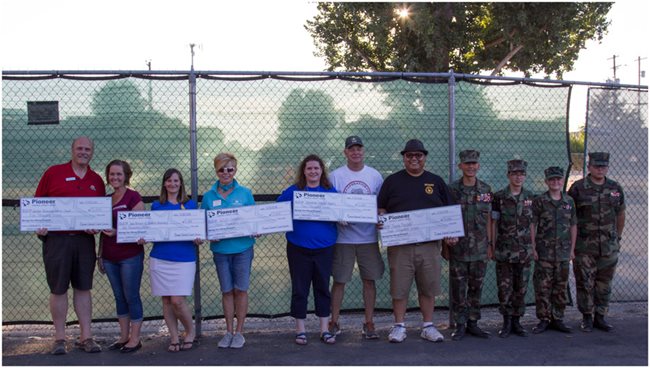 Several people, including kids in military uniforms, with five large checks