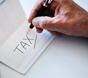 man writing the word TAX on a piece of paper with a pen