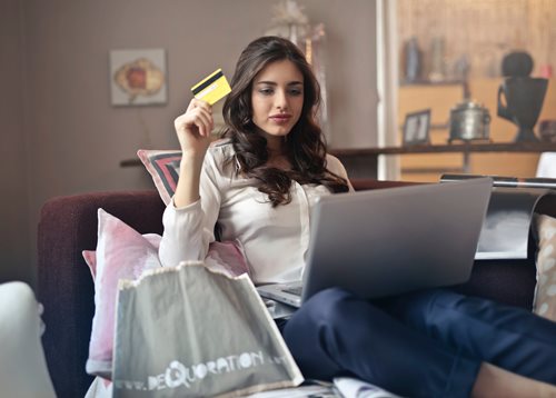young woman sitting on couch online shopping on laptop with credit card in hand