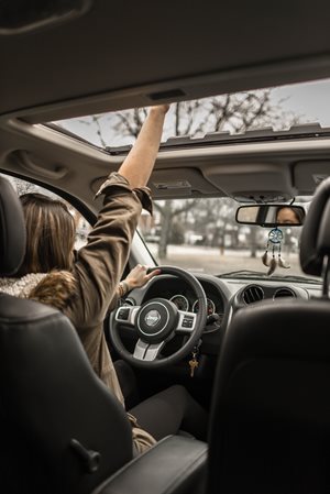woman driving a car and sticking her hand out a sun roof