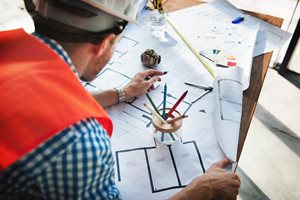 man in orange vest and hard hat sketching architecture
