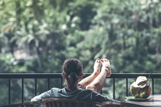 woman with back towards camera sitting and relaxing with a coconut drink next to her