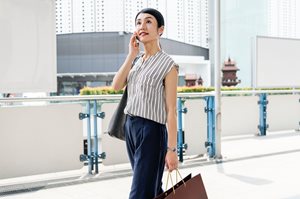 woman walking through store on phone holding a shopping bag