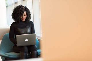 woman sitting in a blue chair working on an Apple laptop