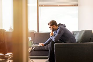 young man sitting on a couch and looking at a laptop