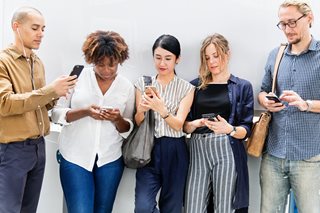 five people of different backgrounds all looking at their smartphones
