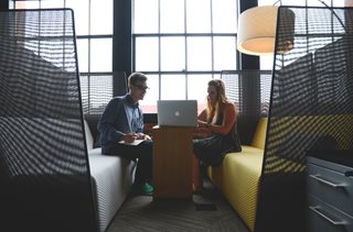 two young people sitting and looking at a laptop and talking