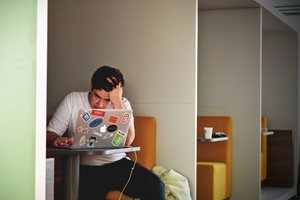 young man looking at a laptop and running his fingers through his hair in frustration