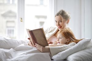 mother reading to young daughter on a bed