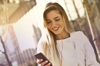 young woman listening to music with earbuds and smiling at her smart phone
