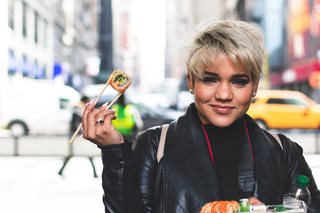 young woman holding a sushi roll in chopsticks in a city