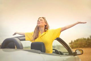 blonde woman with her arms outstretched in a convertible car
