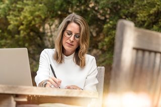 blonde woman writing while sitting outside at a table