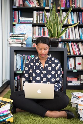young woman looking at a laptop surrounded by books