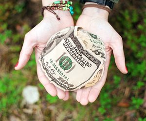 hands holding a large ball of $100 bills