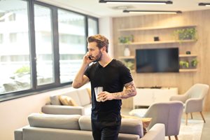 young man walking in his nice home talking on the phone holding a glass of water