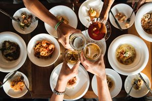 four people clinking glasses together over several dishes of food