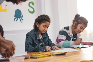 two young girls coloring in a classroom
