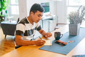 young man sitting at a table and writing on a piece of paper