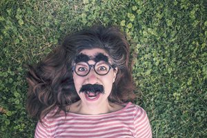 woman laying in the grass wearing a fake mustache and glasses mask
