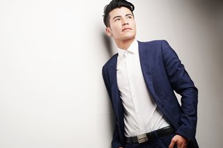 young man wearing a suit leaning against a white wall