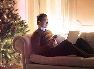 man sitting on couch next to christmas tree while shopping online