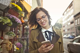 woman outside looking at her phone smiling