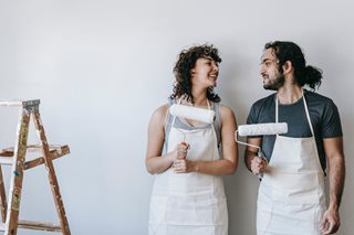 man and woman wearing aprons holding up paint rollers