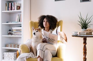 woman sitting in chair with dog reading a newspaper