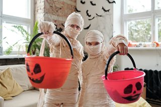 two kids dressed up as mummies with candy buckets