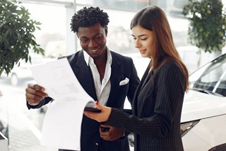man and woman looking at paperwork with a new care behind them