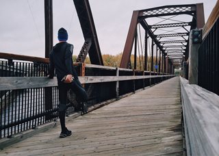 man stretching his legs on a bridge
