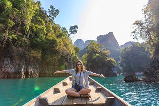 woman sitting on a boat going down a river with big trees